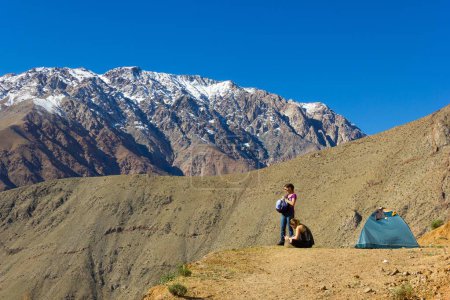 Photo for Couple of blonde girls next to green igloo camping tent with amazing views of Andes snowed mountain range in Elqui Valley, Chile. Backpacker friends, hiking adventure, holidays in nature concepts - Royalty Free Image