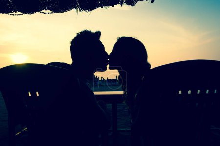 Téléchargez les photos : Silhouette de couple s'embrassant assis sur une cabane près de la plage au coucher du soleil à Goa, en Inde. Style hippie, lune de miel, destination de vacances d'été, concept d'amour. Effet vintage - en image libre de droit