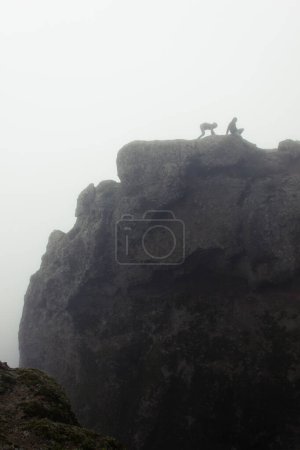 Téléchargez les photos : Les alpinistes inexpérimentés ont du mal à avancer au sommet du rocher de Roque Nublo, Gran Canaria. Silhouette de couple essayant de descendre par une journée dense et brumeuse. Concept de problème - en image libre de droit