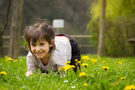 Photo for Adorable little girl leaning on her knees on the green grass surrounded by yellow flowers at park in Bilbao. Young kid in nature, spring time concept - Royalty Free Image