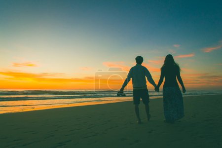 Couple tenant la main marchent pieds nus sur la côte à beau coucher de soleil à Zahora Beach, Andalousie