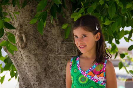 Foto de Niña con colorido vestido de verano bajo el árbol en el parque. Moda para niños, retrato de modelo infantil al aire libre - Imagen libre de derechos