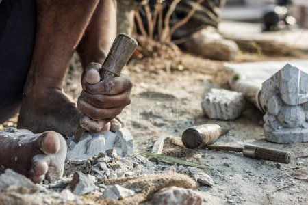 Man barefoot sculpting a rock with a chisel at Chamundi Hills in Mysore, India. Indian sculptor working on street