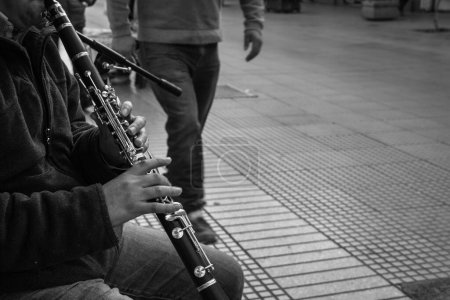 Photo for Hands of young man playing clarinet on street as pedestrian passes by in La Serena city, Chile. Street musician, artist concept - Royalty Free Image