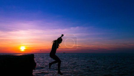 Téléchargez les photos : Silhouette de femme effrayée dans l'air tombant de la falaise dans l'eau au beau coucher de soleil coloré dans l'île de Koh Pha Ngan, Thaïlande. Intrépide, défi, concept d'aventure - en image libre de droit