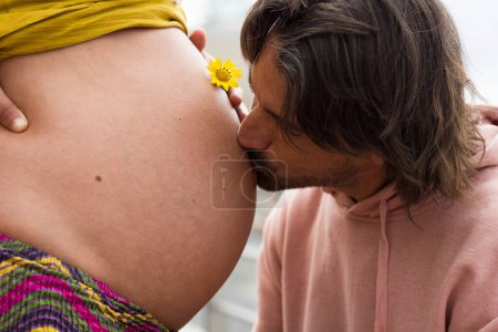 Photo for Dad with long hair kisses mother's big belly. Thrilled father love affection for future baby. New life, parenthood, women's health, wellness, fertility concepts - Royalty Free Image