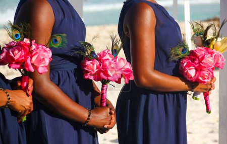 Foto de Tres damas de honor en vestido azul oscuro sosteniendo ramos de rosas en la boda en la playa en Cancún, México. concepto de ceremonia afroamericana - Imagen libre de derechos