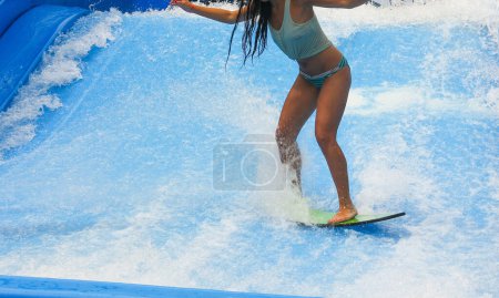 Photo for Young woman in bikini and tank top surfing on wave pool with small board in the island of Phuket, Thailand - Royalty Free Image
