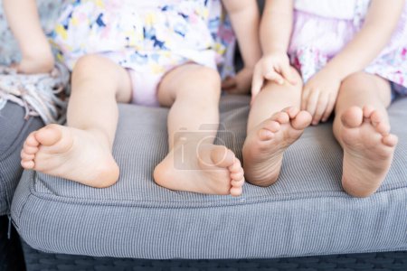 Photo for Bare feet of anonymous little girls resting on couch. Infant twin sisters sitting on sofa. Cozy feeling concept - Royalty Free Image