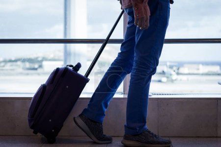 Foto de Hombre en jeans azules caminando con equipaje de mano en la terminal del aeropuerto de Las Palmas. Avión en la zona de aterrizaje cuando pasa el pasajero. Viajes, conceptos de transporte - Imagen libre de derechos