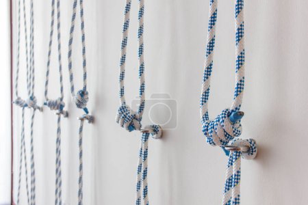Nahaufnahme an blauen und weißen Seilen, die an Metallhaken an der Wand des Yoga-Studios befestigt sind. Yogageräte, Material, Requisiten