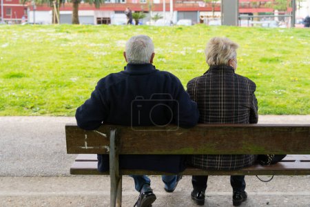 Foto de Detrás de una pareja de ancianos sentados en el banco. Anónimo jubilado marido y mujer hablando en el parque - Imagen libre de derechos