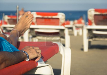 Téléchargez les photos : Homme avec bracelet tout compris au poignet bronzant sur hamac orange sur la plage. Resort, vacances d'été, vacances de voyage, bronzage, soins de la peau, concepts de détente. Effet vintage - en image libre de droit