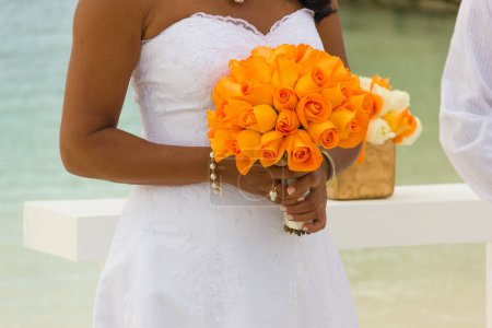 Photo for Bride in white dress holds orange bouquet on the beach. Celebration concept, wedding day - Royalty Free Image