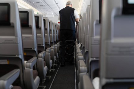 Téléchargez les photos : Un agent de bord qui sert des repas aux passagers dans l'allée de l'avion. Homme anonyme travaillant dans l'avion - en image libre de droit