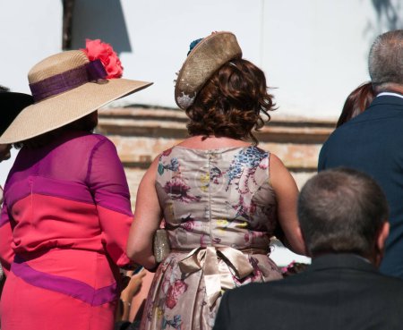 Téléchargez les photos : Retour de gens joliment habillés pour la cérémonie de mariage. Hommes avec tuxedos et femmes avec des robes et des chapeaux colorés élégants - en image libre de droit