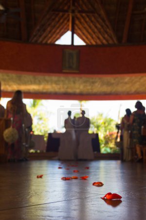 Foto de Primer plano sobre pétalos rojos de flores en el piso de la iglesia y silueta de la pareja de boda casarse en el fondo. Ceremonia religiosa, concepto de día especial - Imagen libre de derechos