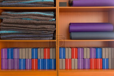 Photo for Front view of wooden stand with yoga props stored nicely. Neat and tidy yoga material placed on wood shelves. Yoga mats, colorful blocks and blankets - Royalty Free Image