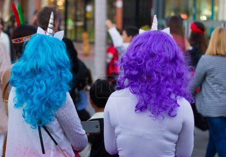 Foto de Parte posterior de las mujeres con pelucas de color azul brillante y púrpura, unicornio en la parte superior viendo desfile de carnaval en la calle. Concepto de evento de celebración - Imagen libre de derechos