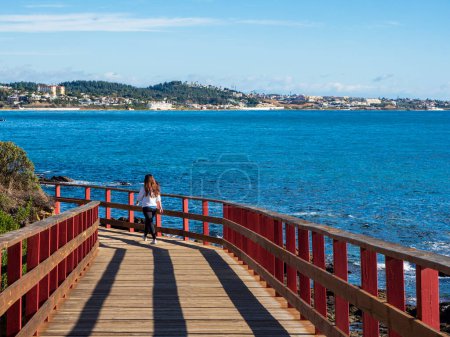   Tourists walking along the wooden path of the coastal path of Mijas on a sunny day.