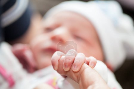 Closeup of a newborn hand and her father finger at hospital on the day of her birth. Fatherhood concept