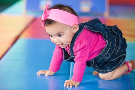 Foto de Hermosa niña de diez meses arrastrándose sobre un fondo colorido. Estimulación temprana para el concepto de niños pequeños. - Imagen libre de derechos