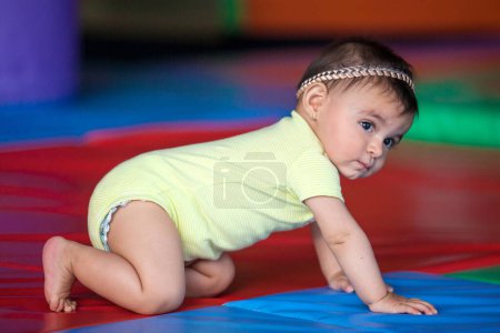 Foto de Hermosa niña de diez meses arrastrándose sobre un fondo colorido. Estimulación temprana para el concepto de niños pequeños. - Imagen libre de derechos