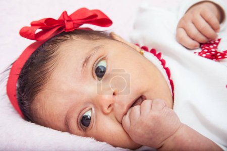 Téléchargez les photos : Gros plan d'une douce petite fille d'un mois avec une expression surprise portant un t-shirt rouge et blanc. - en image libre de droit