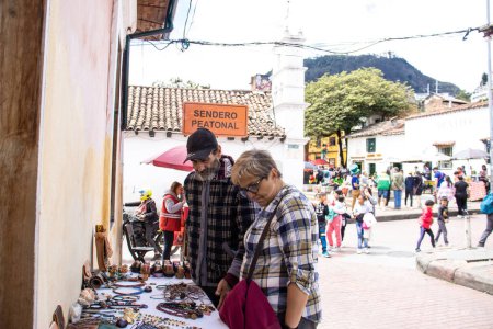Photo for Bogota, Colombia - July 2nd 2023. Tourist buying products from an street artist  at the famous La Candelaria neighborhood at Bogota city center. - Royalty Free Image