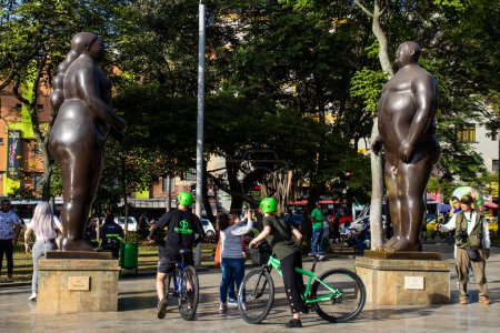 Foto de MEDELLIN, COLOMBIA - 17 DE ENERO DE 2024: Adán y Eva. Turista en bicicleta en la plaza Fernando Botero en el centro de la ciudad de Medellín. Escultura de Adan y Eva. - Imagen libre de derechos