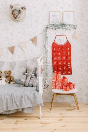 Téléchargez les photos : Beau calendrier de l'Avent rouge sur le mur dans la chambre des enfants avec beaucoup de jouets, de lumières et de cadeaux de Noël rouges. Photo de haute qualité - en image libre de droit