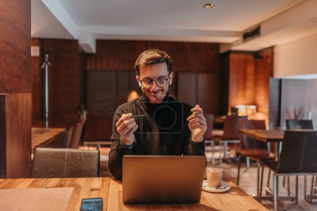 Foto de Happy young businessman working on a laptop in a cafe. - Imagen libre de derechos