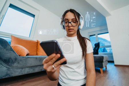 Foto de Una mujer que usa un teléfono inteligente mientras hace varios ejercicios en casa, rodeada de hologramas que muestran su estado de salud. Convergencia de la tecnología y ejercicio en el hogar, destacando la importancia - Imagen libre de derechos