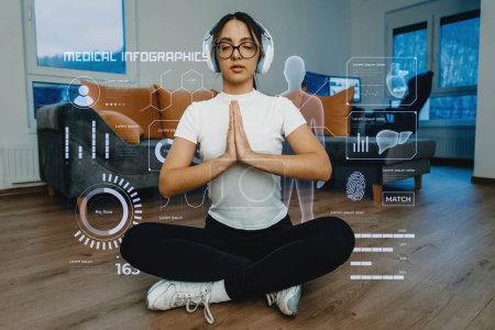Foto de Una mujer que usa un teléfono inteligente mientras hace varios ejercicios en casa, rodeada de hologramas que muestran su estado de salud. Convergencia de la tecnología y ejercicio en el hogar, destacando la importancia - Imagen libre de derechos