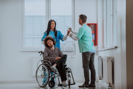 El médico y una enfermera discuten la salud de los pacientes mientras el paciente, que está en silla de ruedas, está presente junto a ellos.