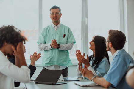 Photo for A team of doctors and a medical nurse applauding their colleague after a presentation in a meeting room. - Royalty Free Image