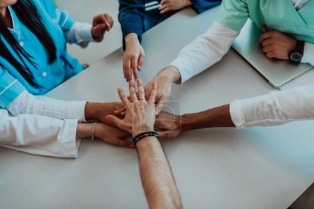 Eine Gruppe von Ärzten und eine Krankenschwester legen ihre Hände an einen Tisch und zeigen damit die unerschütterliche Teamarbeit und Solidarität, die ihre gemeinsamen Bemühungen im Gesundheitsbereich antreiben..