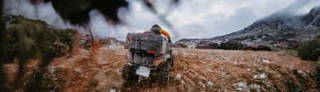 Photo for Wide photo of a man is fearlessly enjoying an adventurous ride on an ATV Quad through hazardous snowy terrain, embracing the thrill and excitement of the challenging mountainous landscape. - Royalty Free Image