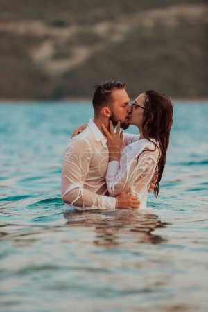 Foto de Una romántica pareja joven compartiendo un beso apasionado en medio de la serena belleza del océano al atardecer - Imagen libre de derechos