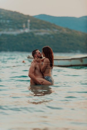 Foto de Una romántica pareja joven compartiendo un beso apasionado en medio de la serena belleza del océano al atardecer - Imagen libre de derechos