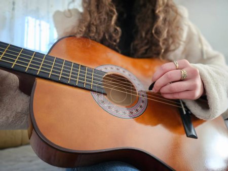 Foto de La joven de pelo rizado toca su guitarra acústica con pasión y talento en la comodidad de su hogar, creando bellas melodías en esta fotografía realista. - Imagen libre de derechos