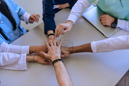 Foto de Un grupo de médicos y una enfermera médica unen sus manos en una mesa, mostrando el trabajo en equipo inquebrantable y la solidaridad que impulsa sus esfuerzos colectivos en el campo de la salud. - Imagen libre de derechos