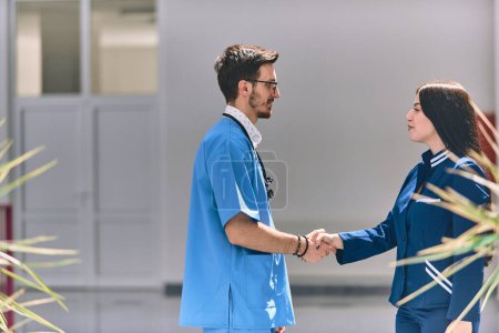 Photo for A doctor and a nurse share a friendly handshake in the hallway of a large, modern hospital, symbolizing collaboration, trust, and dedication in healthcare. - Royalty Free Image