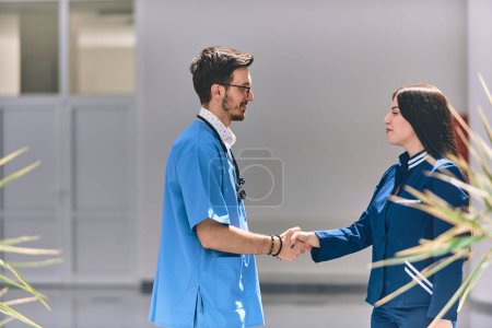 Photo for A doctor and a nurse share a friendly handshake in the hallway of a large, modern hospital, symbolizing collaboration, trust, and dedication in healthcare. - Royalty Free Image