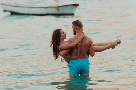 A handsome man tenderly holds his girlfriend in his arms while standing in the sea during the enchanting sunset, capturing a moment of muscular strength and affectionate romance against the backdrop