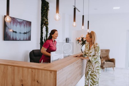 A beautiful blonde woman conversing with the dental clinic receptionist, scheduling an appointment for dental treatment with a bright smile. 