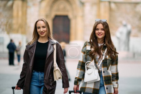 Zwei Touristinnen erkunden eine europäische Stadt, ziehen ihre Koffer mit, während sie durch die charmanten Straßen schlendern und in die Kultur und Schönheit ihres Reiseziels eintauchen..