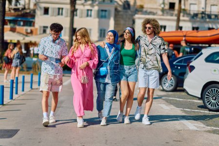 Photo for A diverse group of tourists, dressed in summer attire, strolls through the tourist city with wide smiles, enjoying their sightseeing adventure. - Royalty Free Image