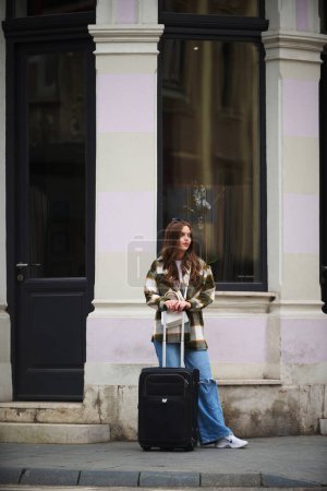 Eine schöne Frau mit einem Koffer geht auf eine touristische Reise in europäische Städte, Konzept des Tourismus, eine sexy Frau geht zu modernen touristischen Orten, eine Frau genießt die Straßen einer modernen europäischen Stadt. 