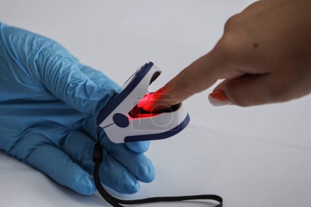 Foto de Médico examinando paciente con oxímetro de pulso en la punta de los dedos en la mesa de madera blanca, primer plano. Foto de alta calidad - Imagen libre de derechos